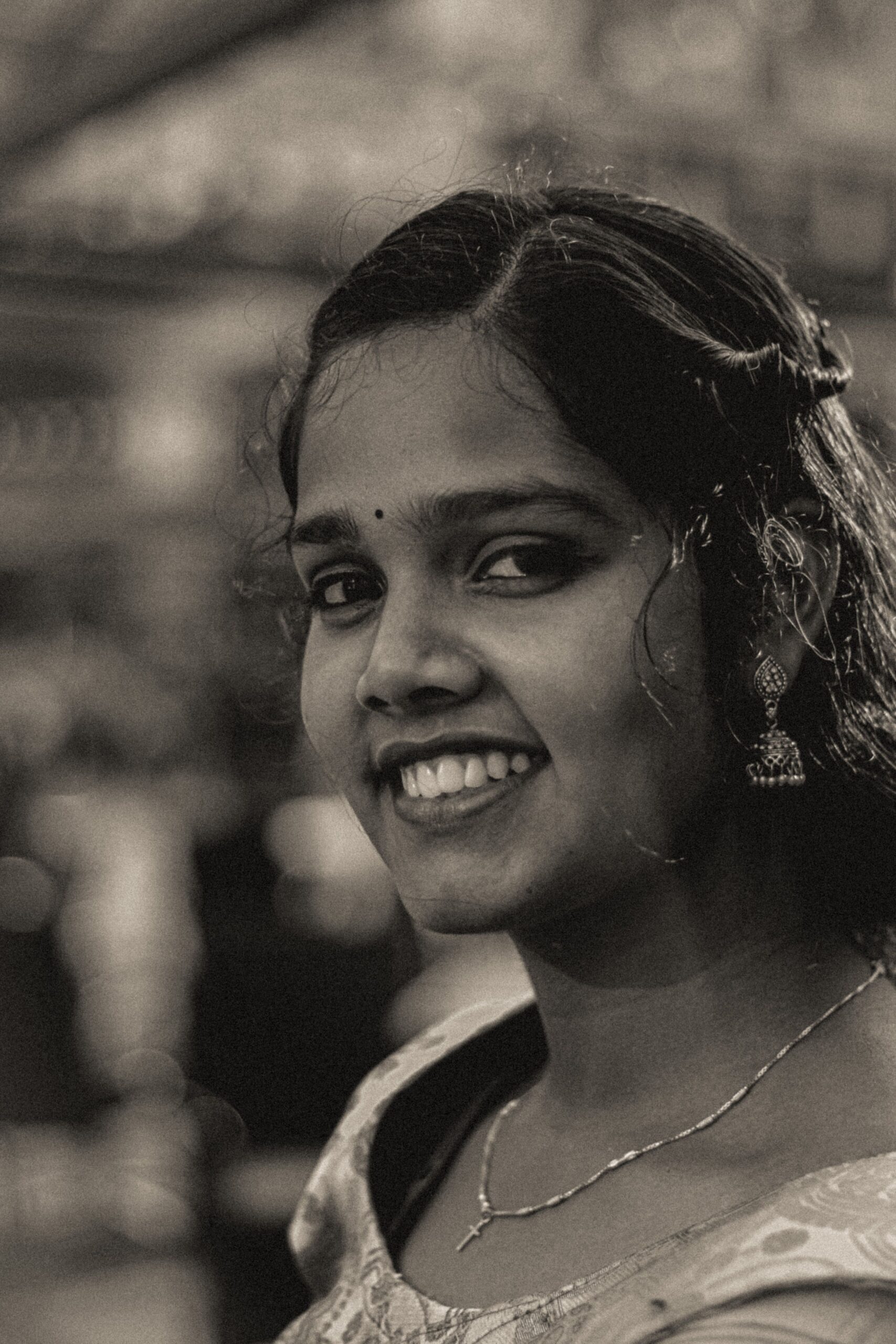 Black and white portrait of a young woman smiling, showcasing traditional jewelry and attire.