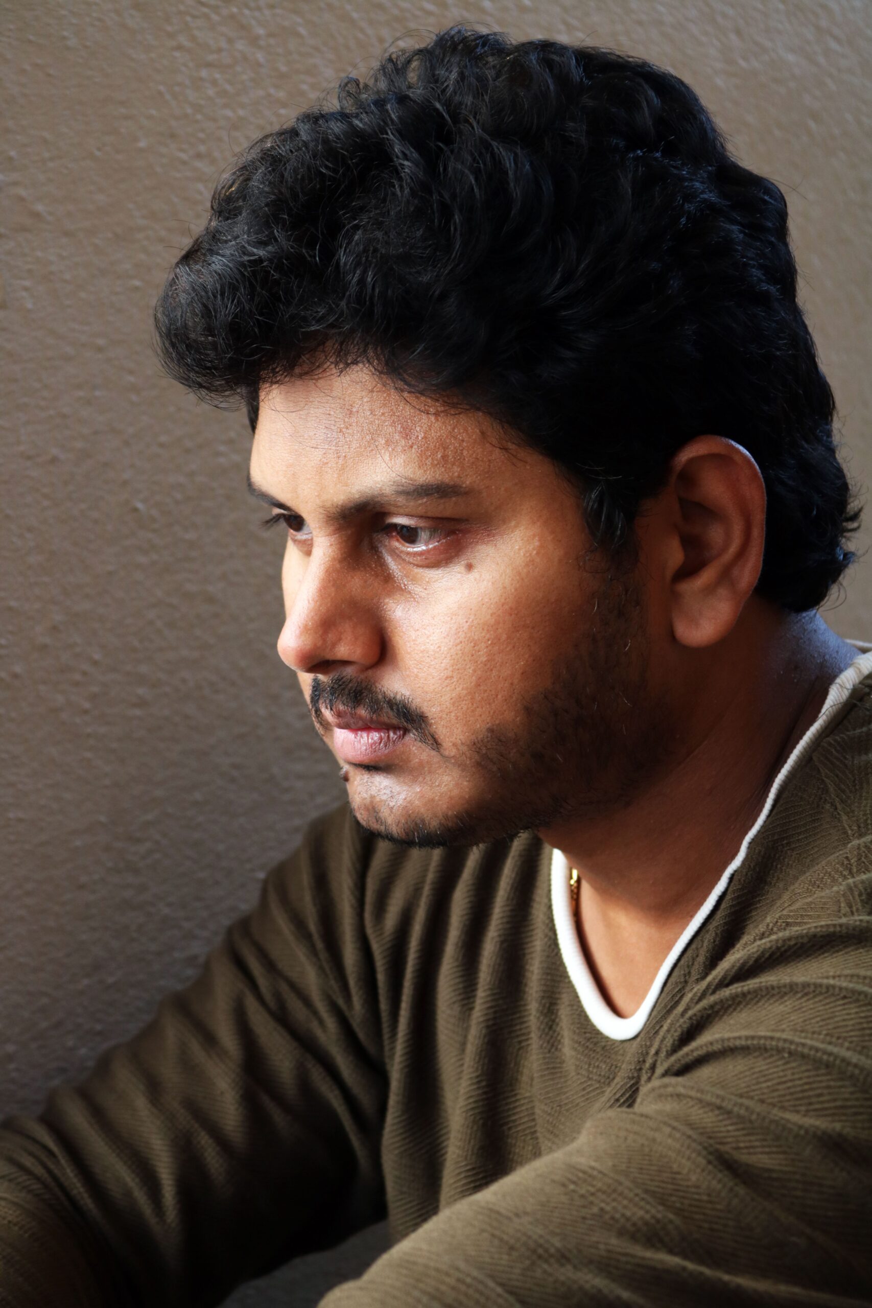 Close-up of a thoughtful South Asian man with short black hair indoors.